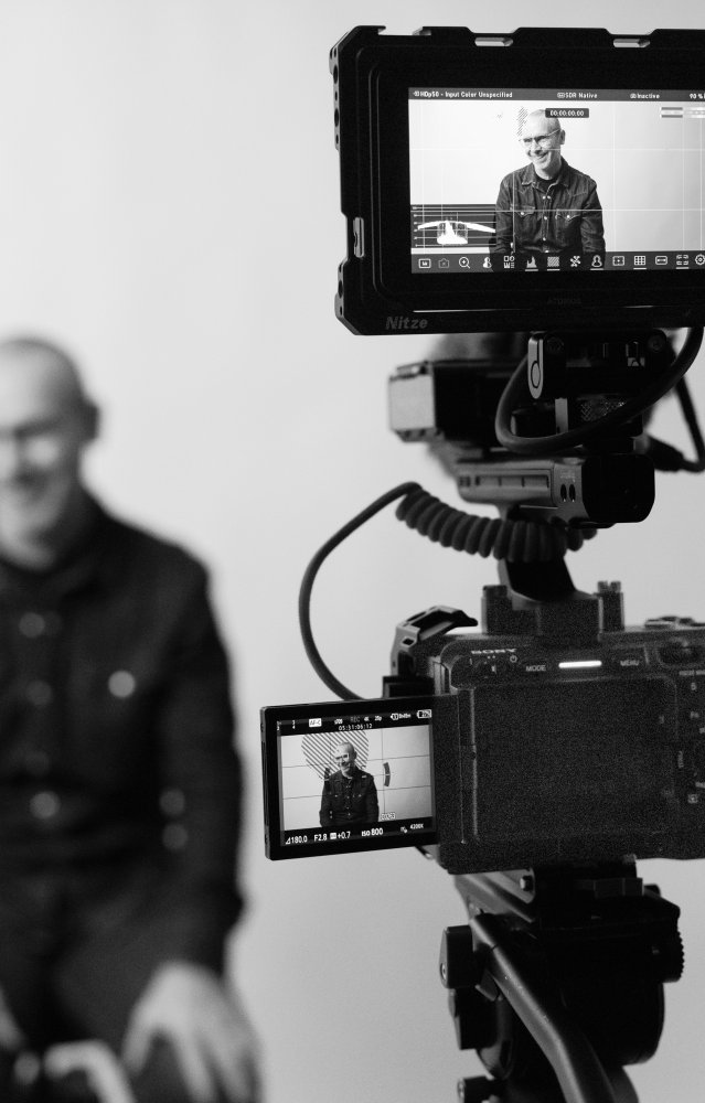 Scène avec en arrière-plan une personne interviewée, et au premier plan, la caméra en marche.